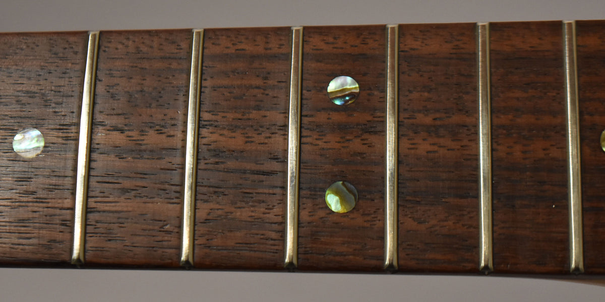 Close-up of a dark rosewood fretboard with five frets and three iridescent abalone dot inlays, showing light wear.