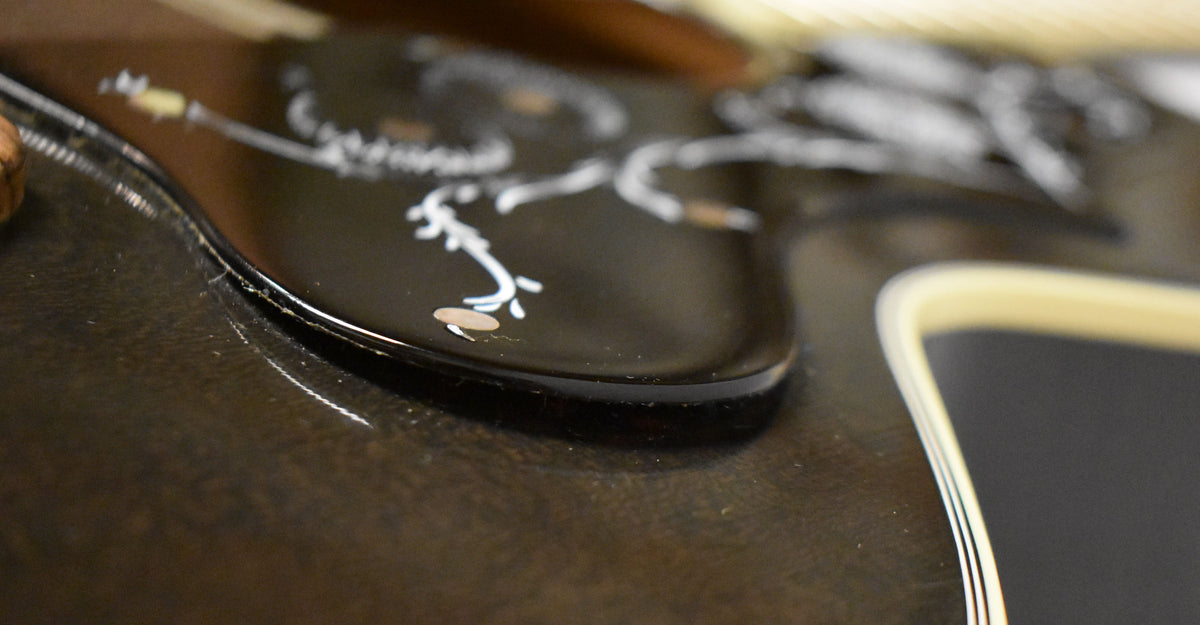 Close-up of the black pickguard with white floral inlay, showing finish wear and light scratches on the guitar's dark body.