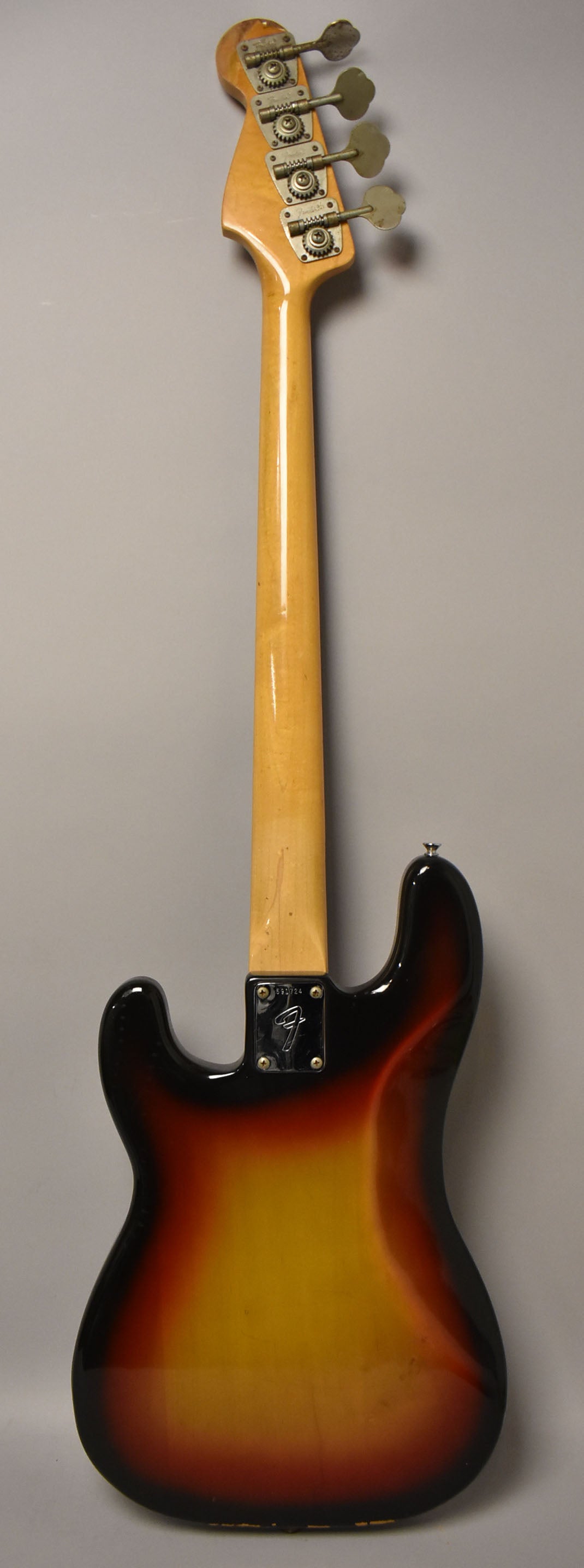 Full rear view of a sunburst bass, showing the maple neck, headstock with four clover-leaf tuners, and neck plate.