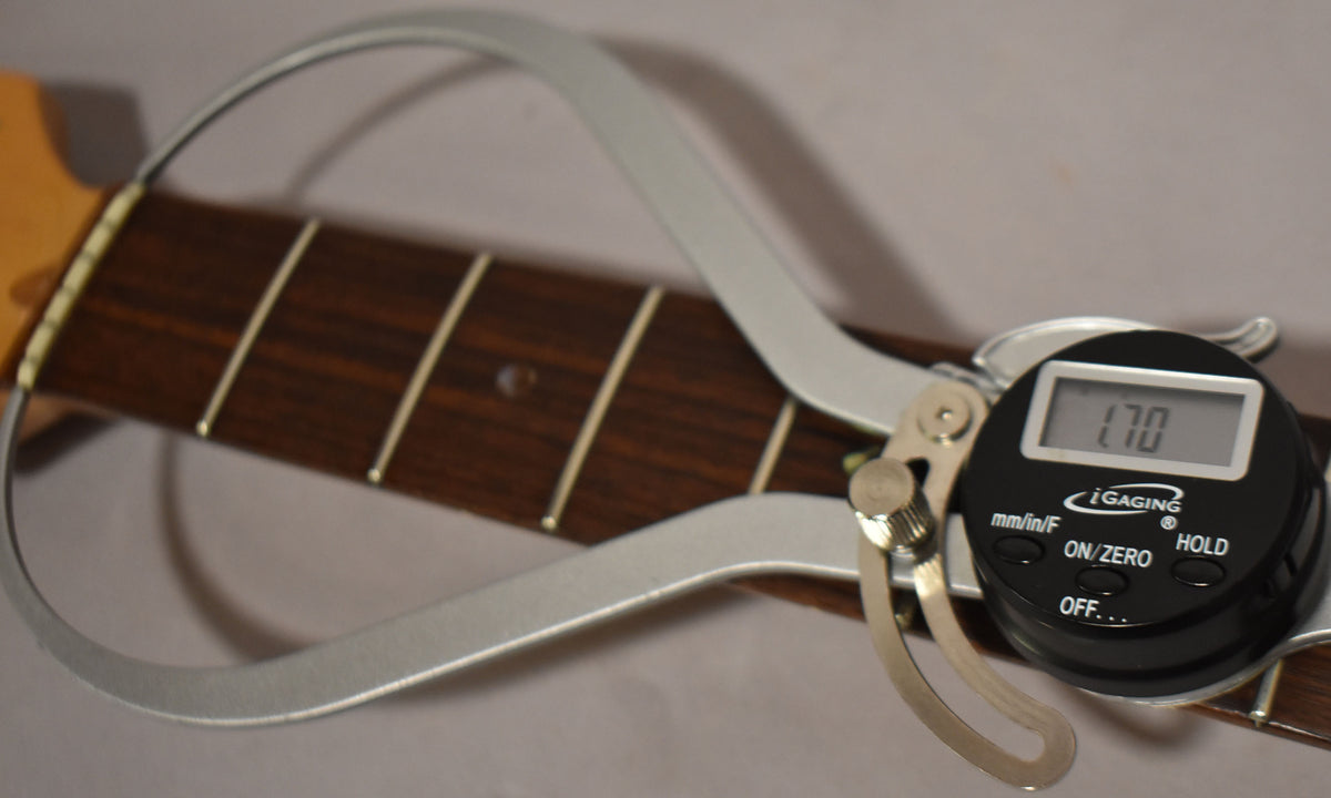 Close-up of the dark rosewood fretboard with a digital caliper measuring the fret width at 1.70 inches.