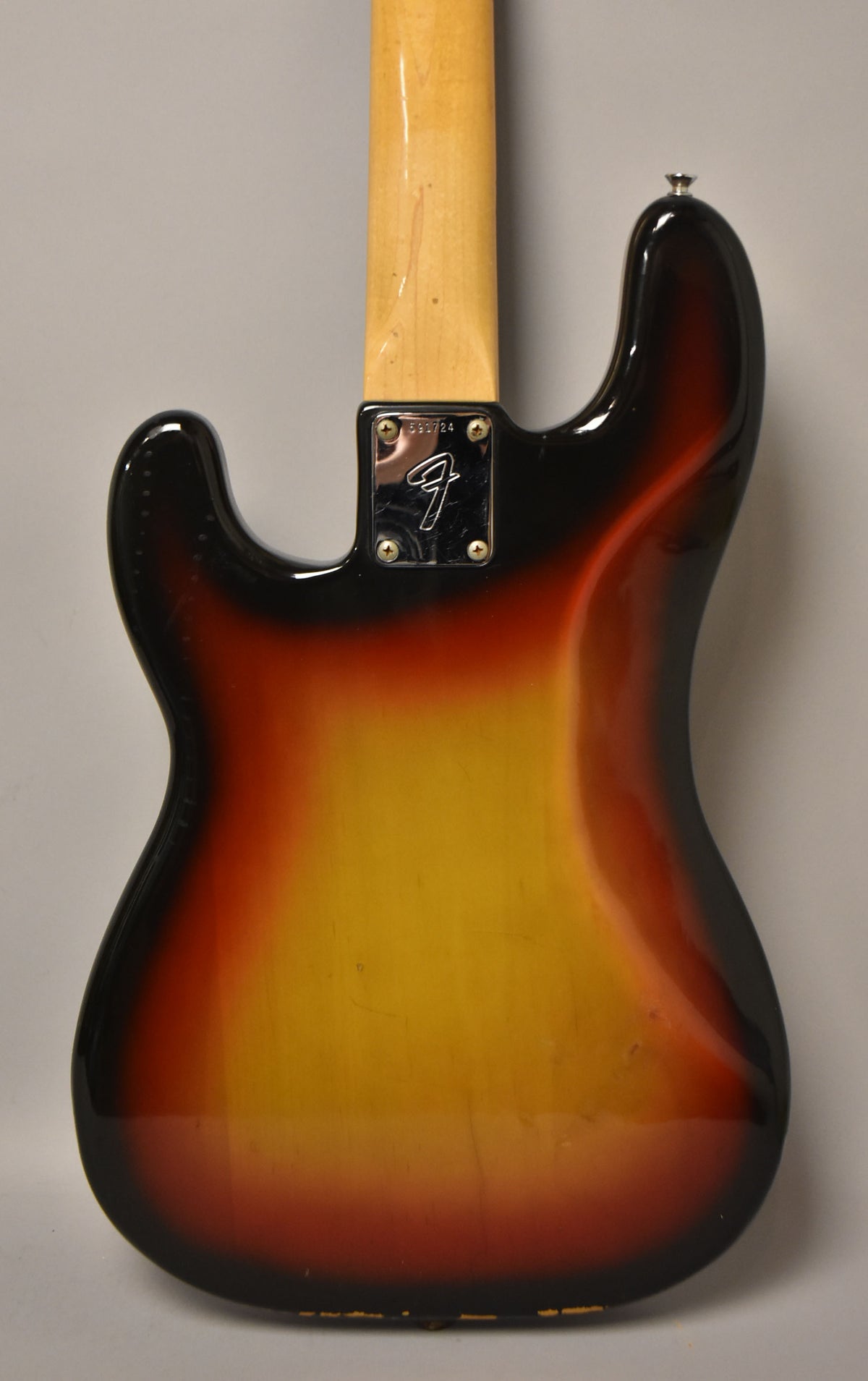 The bass guitar's sunburst back shows a chrome neck plate, a light wood neck, and wear along the bottom edge.