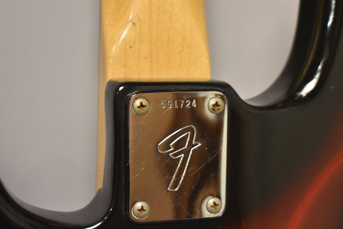 Close-up of the bass's neck plate, showing a chrome finish with light scratches, four screws, and the serial number 591724.