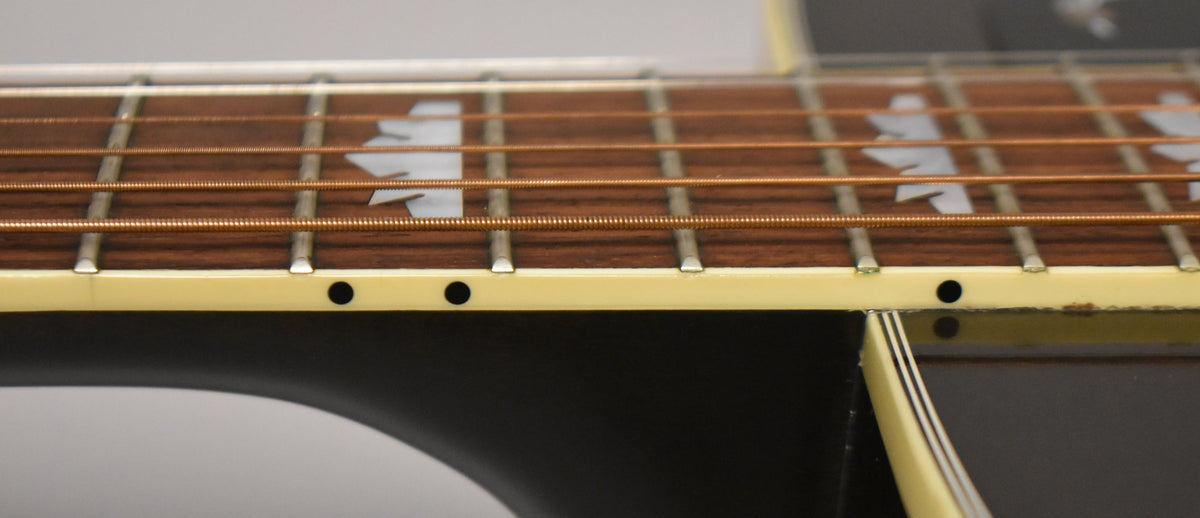 Close-up of the guitar's fretboard, showing copper strings, white maple leaf inlays, and cream binding with side dots.