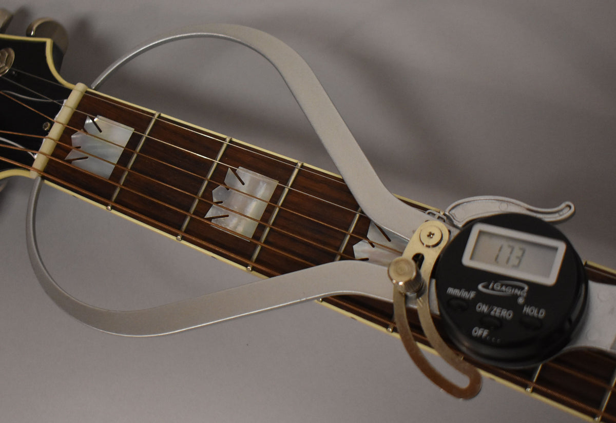 A digital caliper measures the guitar's nut width at 1.73 inches, resting on the dark rosewood fretboard with mother-of-pearl inlays.