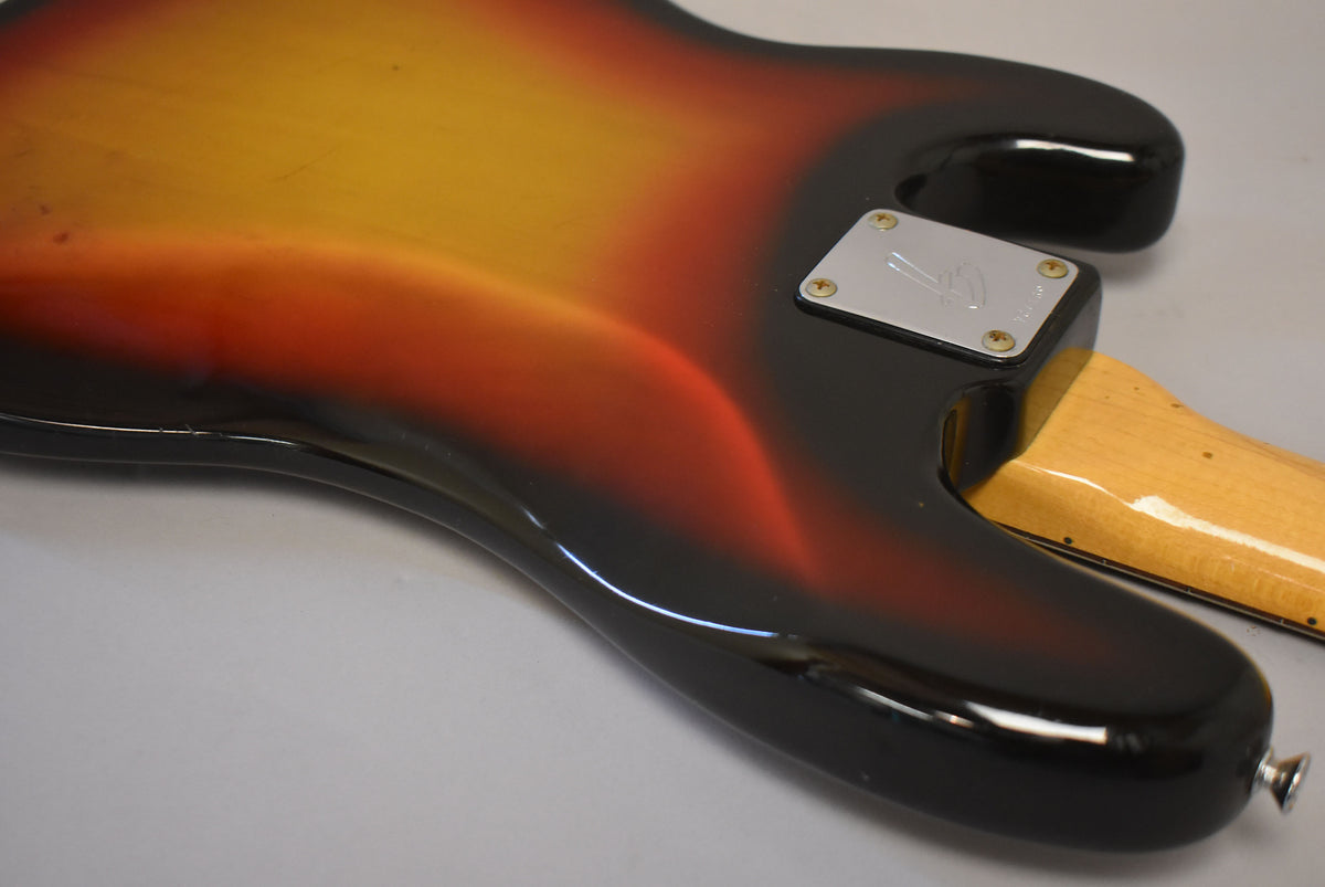 The bass's sunburst body, showing wear and checking, angles from the neck plate to the strap button, revealing a worn maple neck.