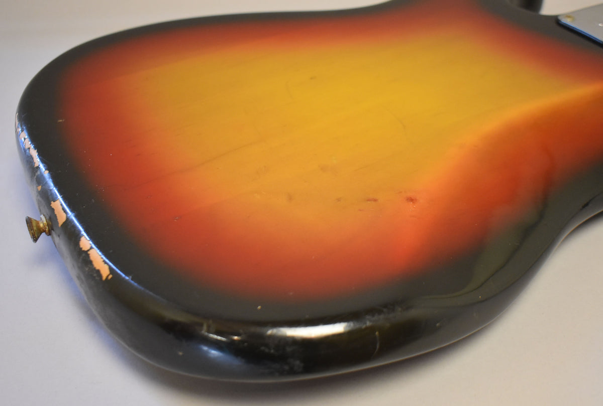 Close-up of the bass's sunburst body, showing heavy wear and paint chips along the bottom edge and light scratches on the back.