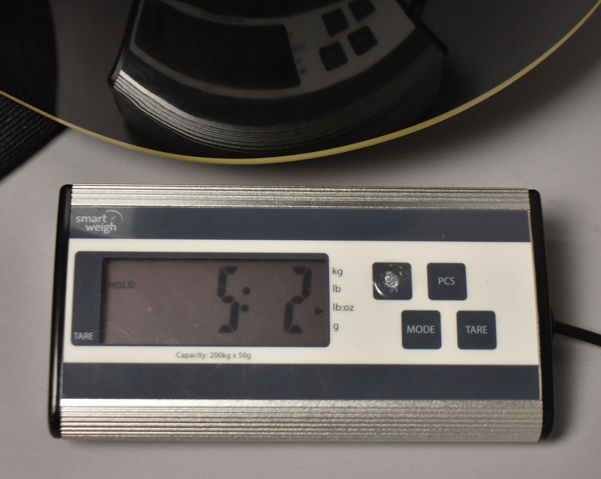 A digital scale displays "5.2" lbs, with a partial view of the guitar's black body and a yellow string above.