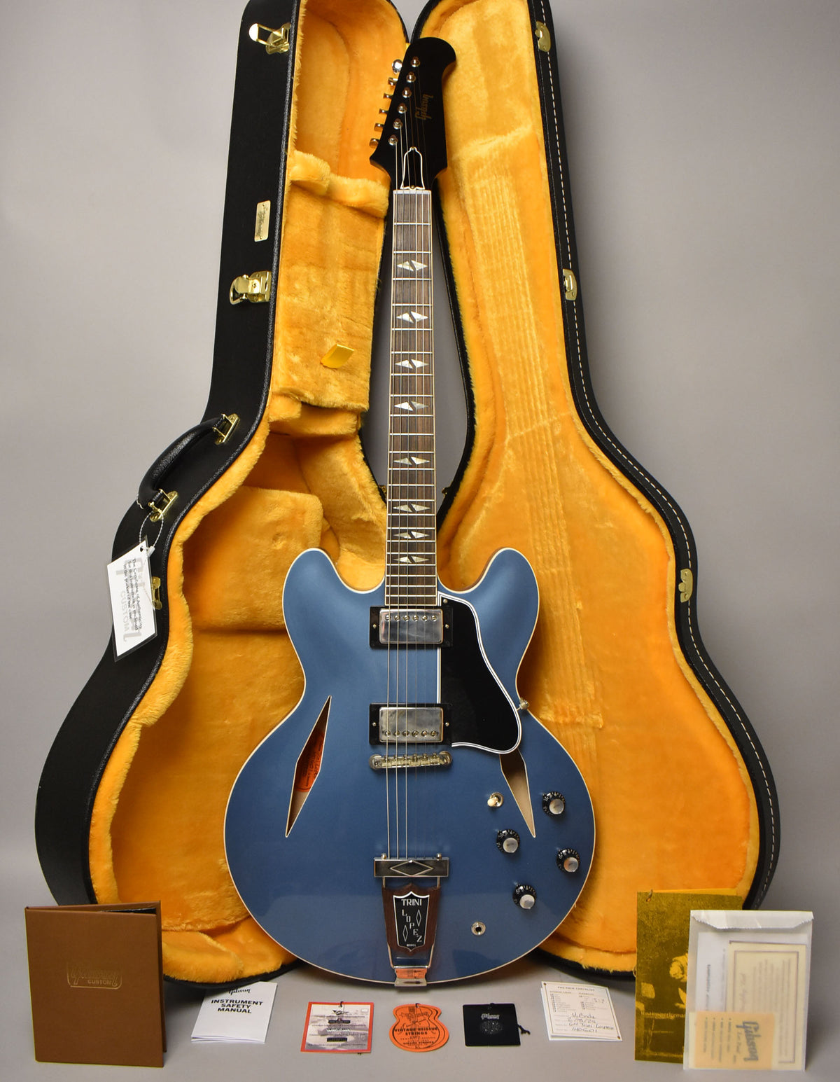 Full view of a Pelham Blue semi-hollowbody electric guitar with a black pickguard, two humbuckers, and a Trini Lopez tailpiece, resting in its open, yellow-lined hard case.