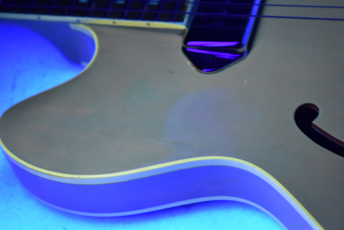 Close-up of the guitar's lower bout and f-hole, showing the cherry finish under blue light, with binding and light surface wear.