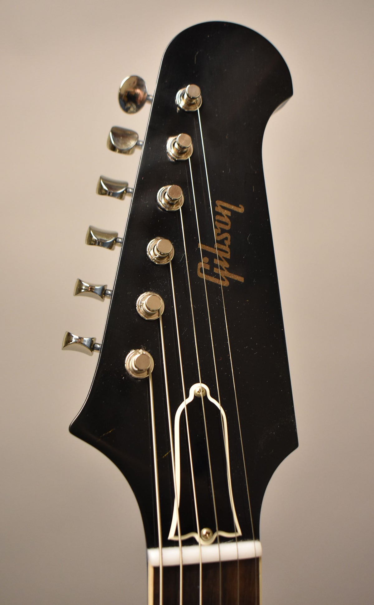Close-up of a black headstock with six chrome tuners, a white nut, and a white bell-shaped truss rod cover.