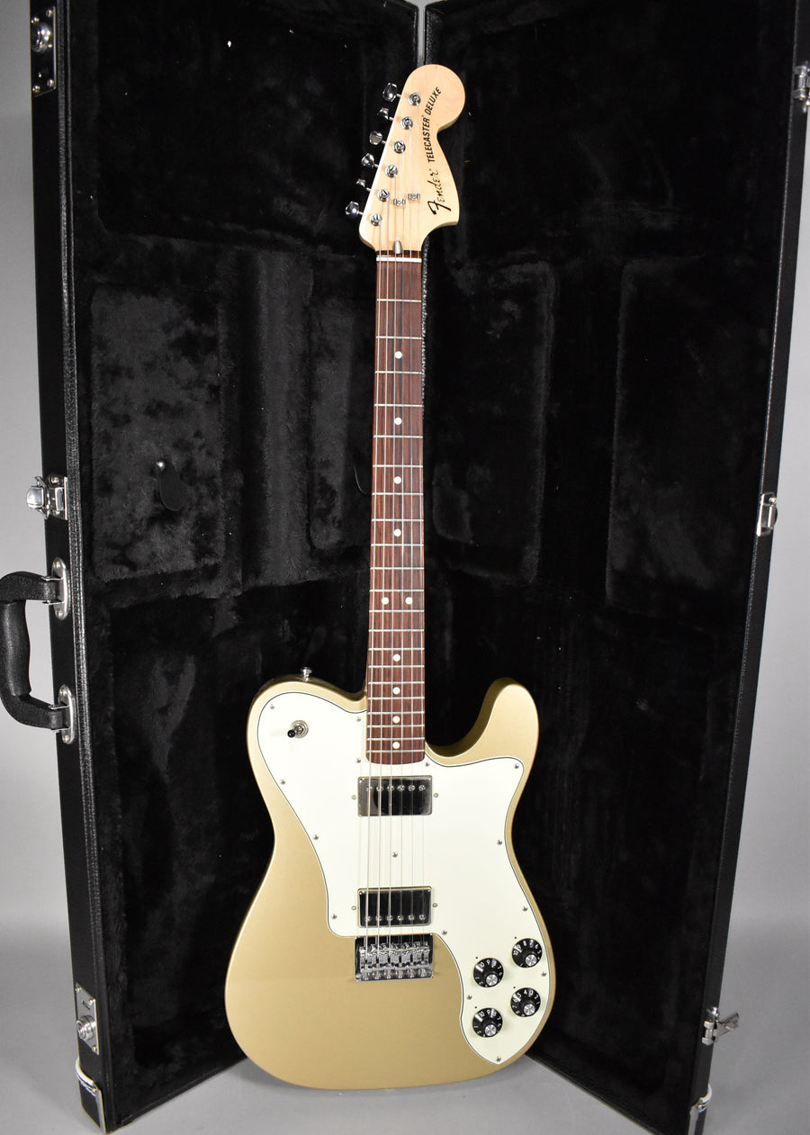 Full-length view of a gold Telecaster Deluxe with a white pickguard, two humbuckers, and four black control knobs, in its open black hard case.