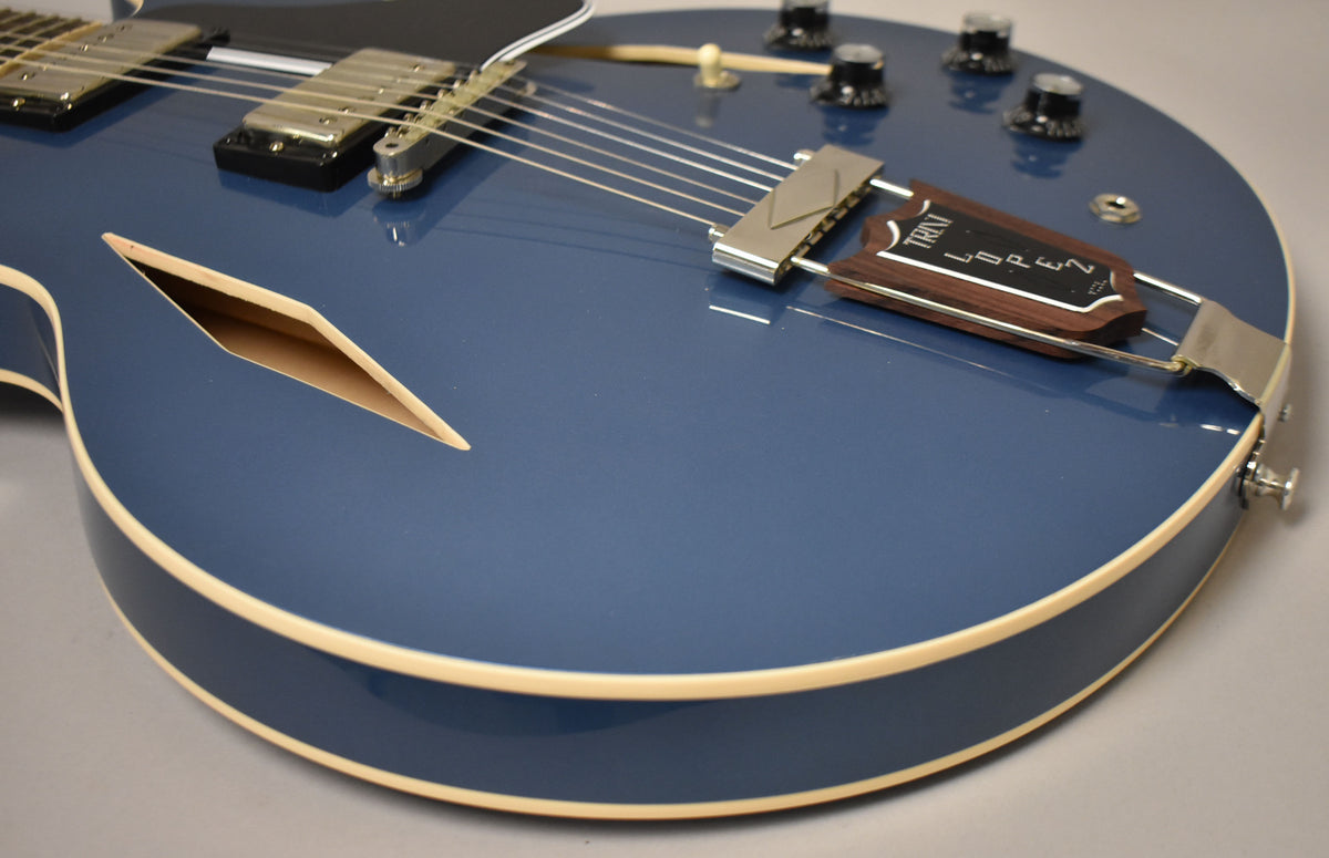 Close-up of a Pelham Blue semi-hollow guitar body, showing the diamond f-hole, chrome pickups, and a Trini Lopez trapeze tailpiece.