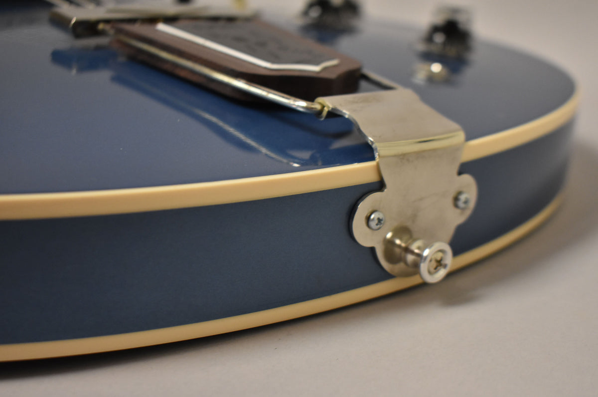 Close-up of the guitar's lower bout, showing the Pelham Blue finish, cream binding, and chrome trapeze tailpiece with strap button.