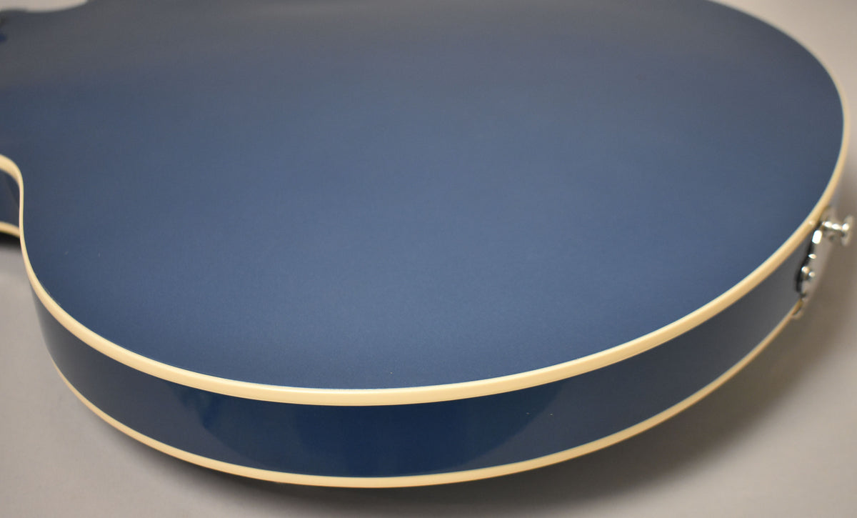 Close-up of the guitar's lower bout, showing the Pelham Blue finish, cream binding, and a chrome strap button on the side.