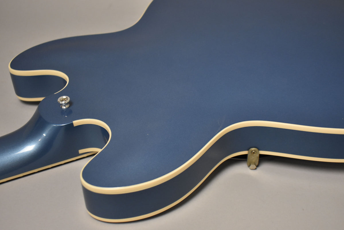 The guitar's lower bout and neck heel are visible, showing the Pelham Blue finish with cream binding and two strap buttons.