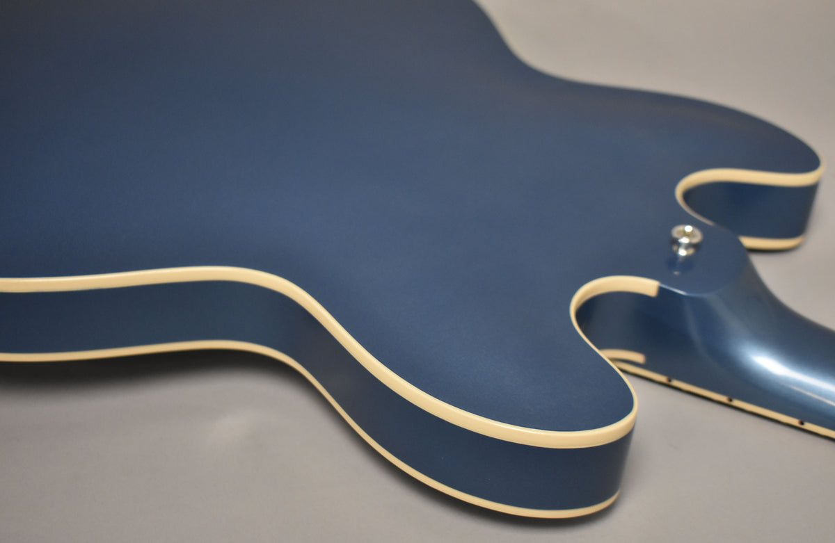 The upper bout and cutaways of a Pelham Blue guitar with cream binding, showing a matte body and glossy neck heel.