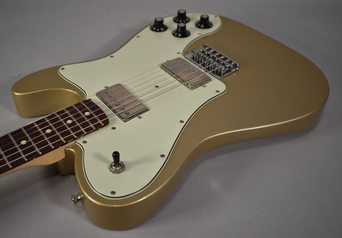Angled view of a gold guitar with a cream pickguard, two chrome humbuckers, a chrome bridge, and four black control knobs.