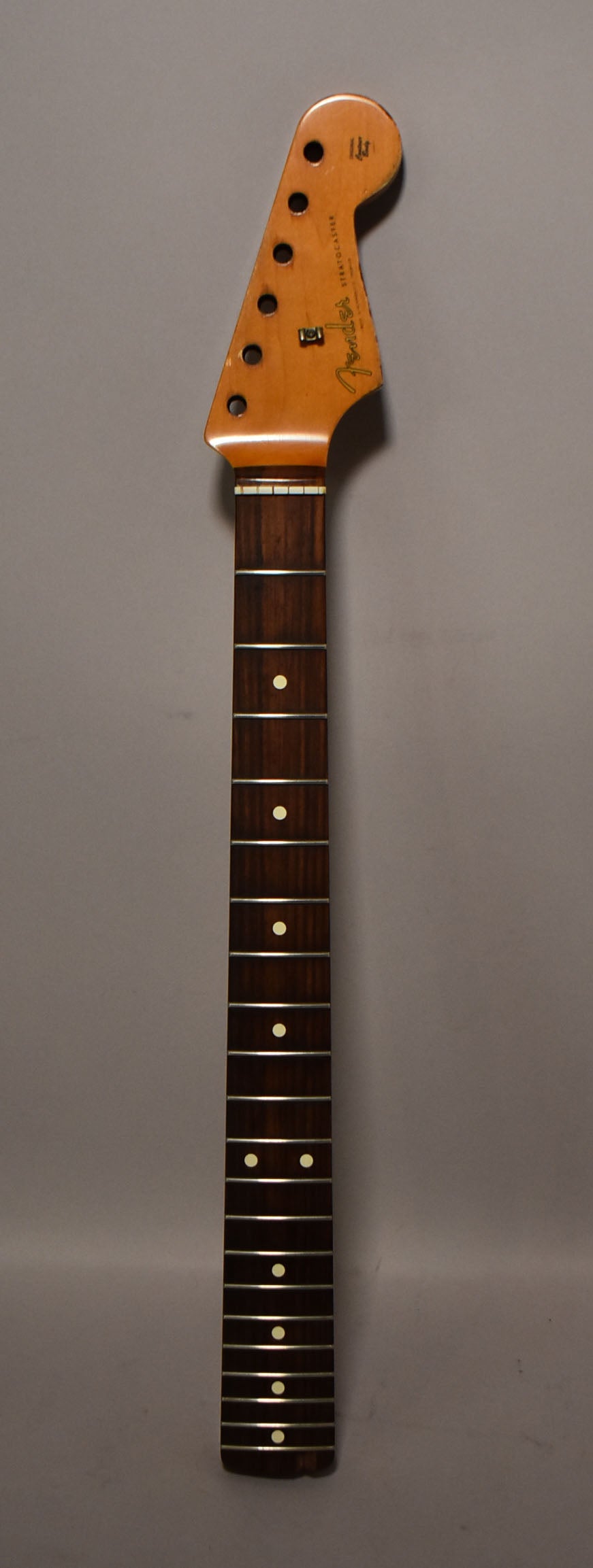 Full view of a relic'd maple guitar neck with a dark rosewood fretboard, showing six tuner holes and cream dot inlays.