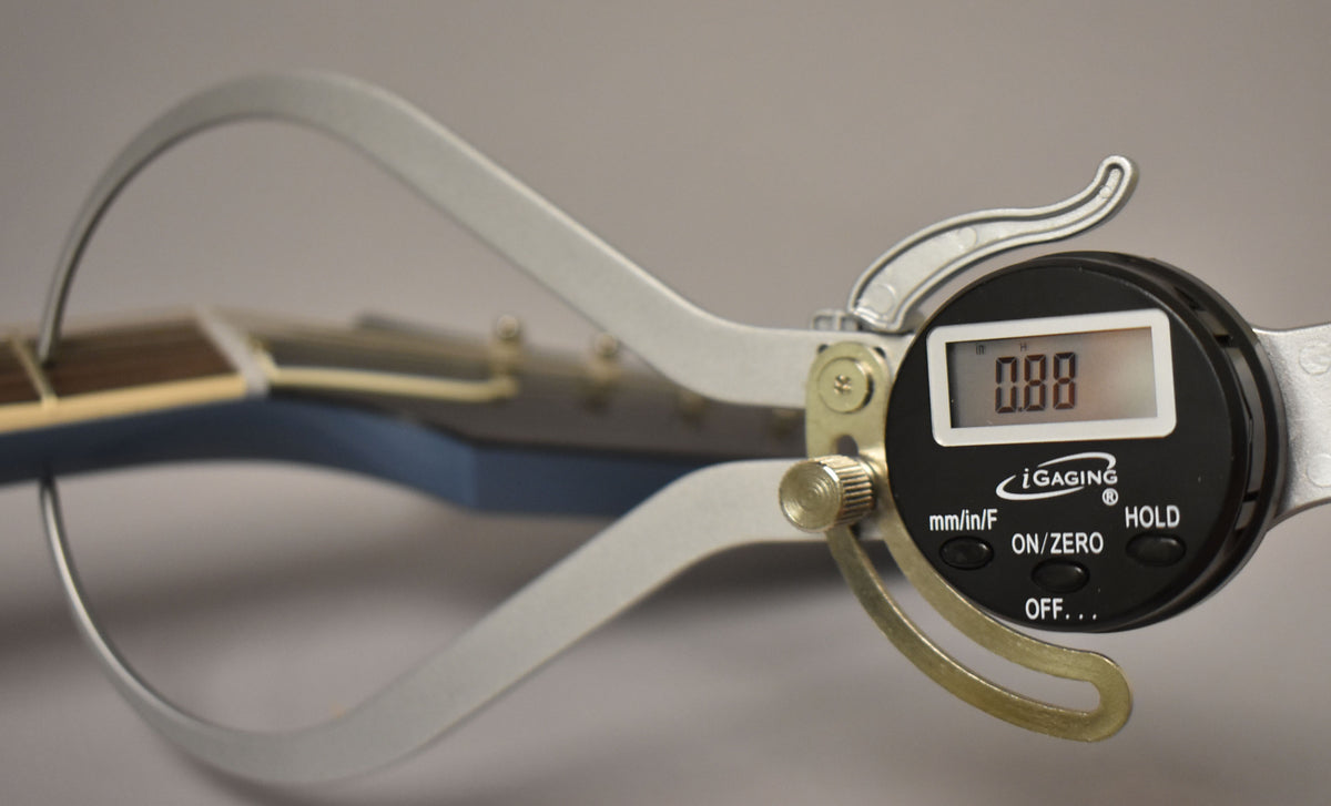 A digital caliper measures the Pelham Blue guitar's neck thickness, showing "0.88" on its screen.