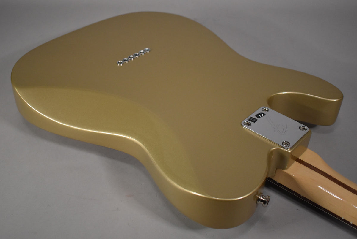 The back of a metallic gold guitar body, showing the chrome neck plate, string-through-body ferrules, and output jack.