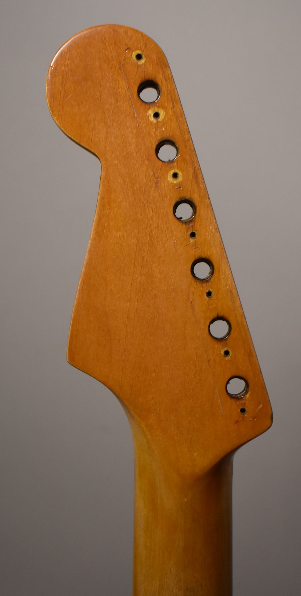 The front of a light brown guitar headstock and upper neck, showing six tuner holes with visible wear and screw holes.
