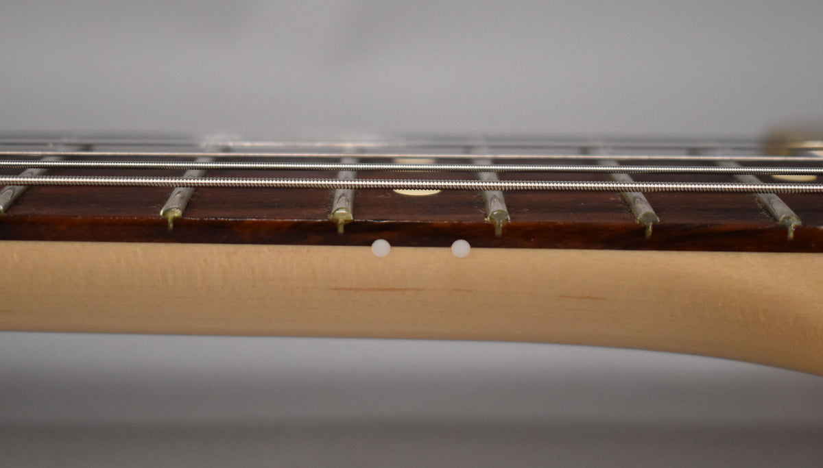Close-up of the guitar's fretboard and neck, showing two white side dot markers and light wear on the frets and dark wood.
