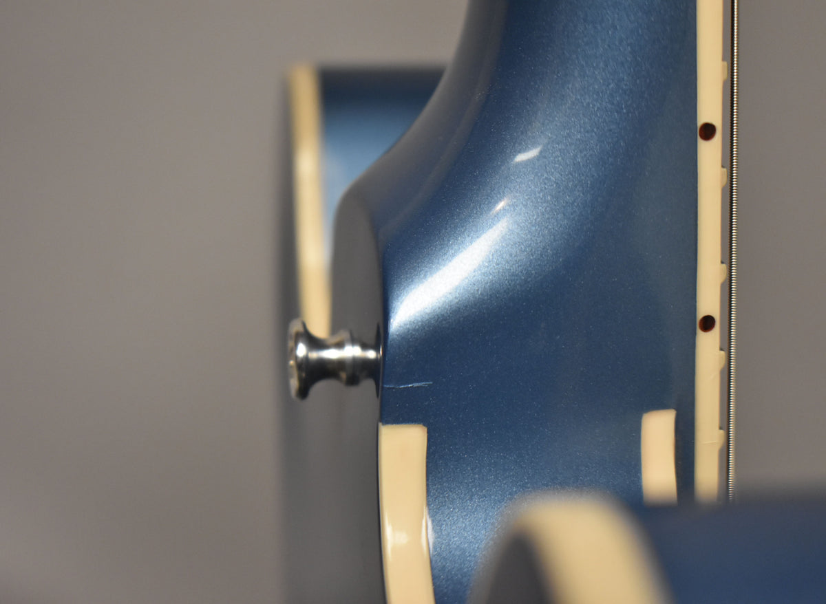 Close-up of the Pelham Blue guitar's neck heel and lower bout, showing a chrome strap button and a small scratch on the finish.