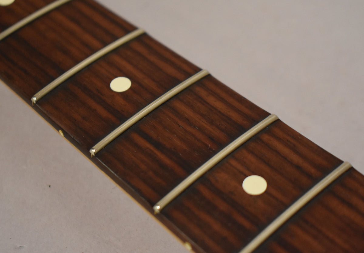 Close-up of the dark rosewood fretboard with light cream dot inlays and shiny frets, showing light wear and grain.