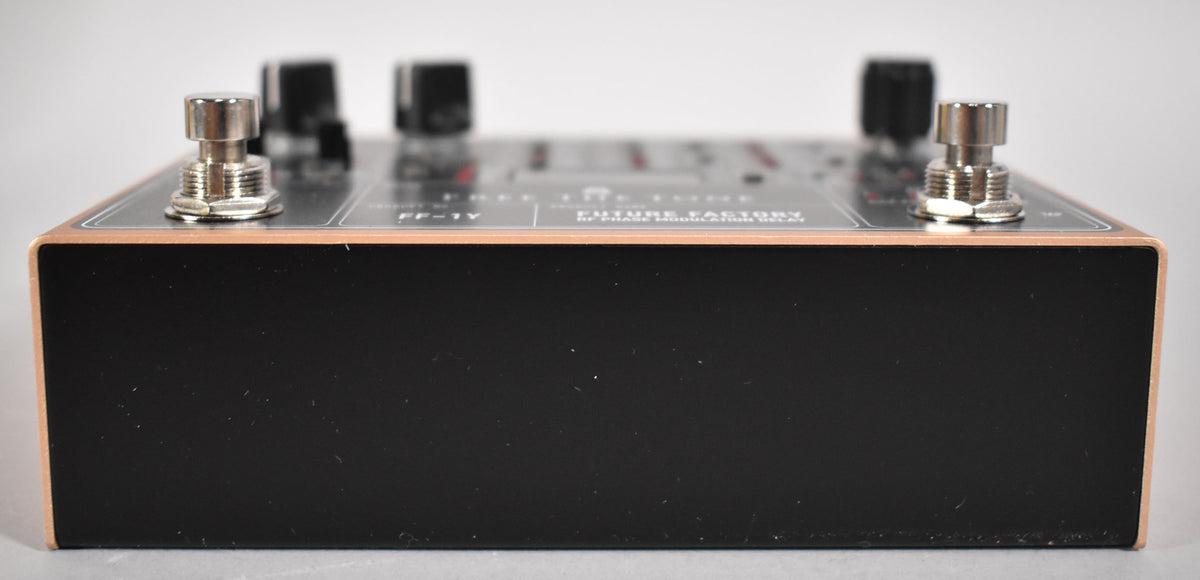 The delay pedal is viewed from the side, showing its black body, copper-colored top edge, and two silver footswitches.