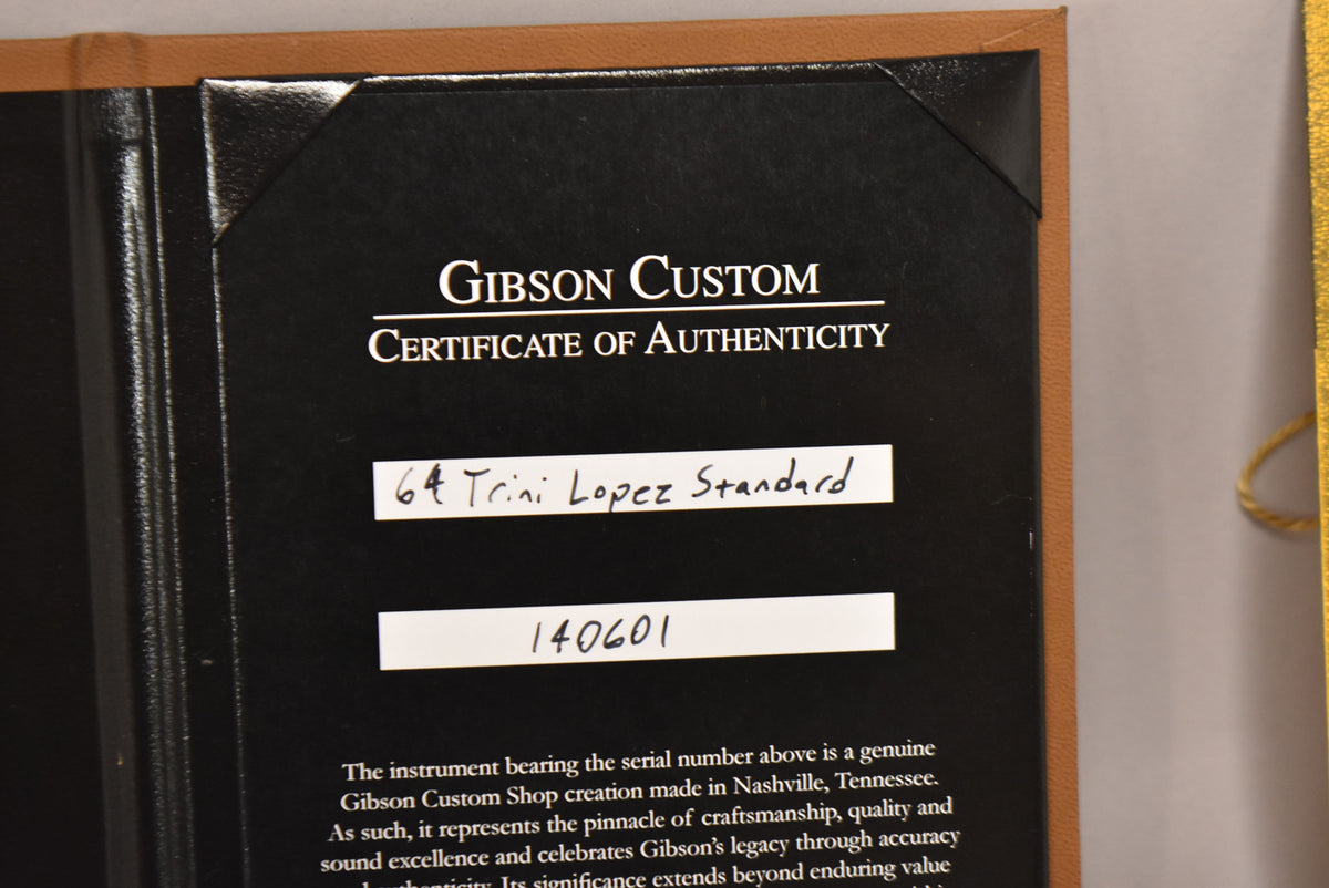 Close-up of the black Gibson Custom Certificate of Authenticity, with "64 Trini Lopez Standard" and "140601" handwritten on white labels.