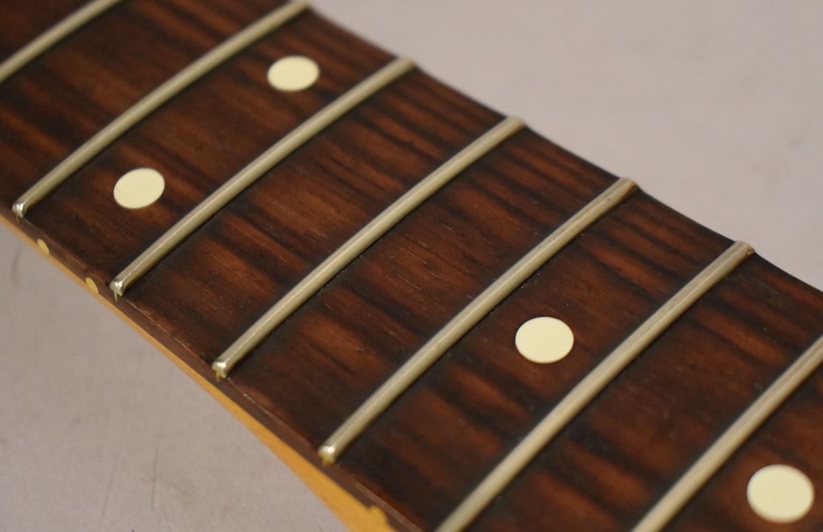 Close-up of the dark rosewood fretboard with cream dot inlays and light fret wear, angled from the lower left.