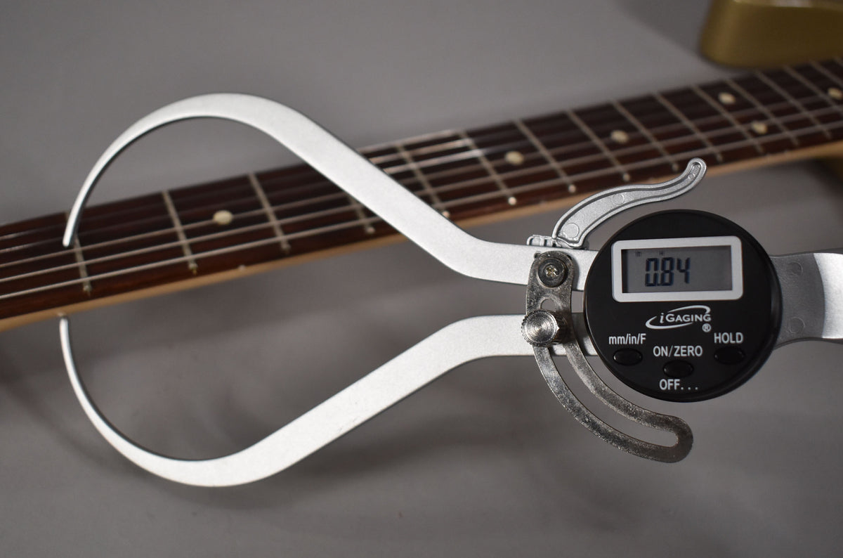 A digital caliper measures the fret height at 0.04 inches on the dark rosewood fretboard with dot inlays.