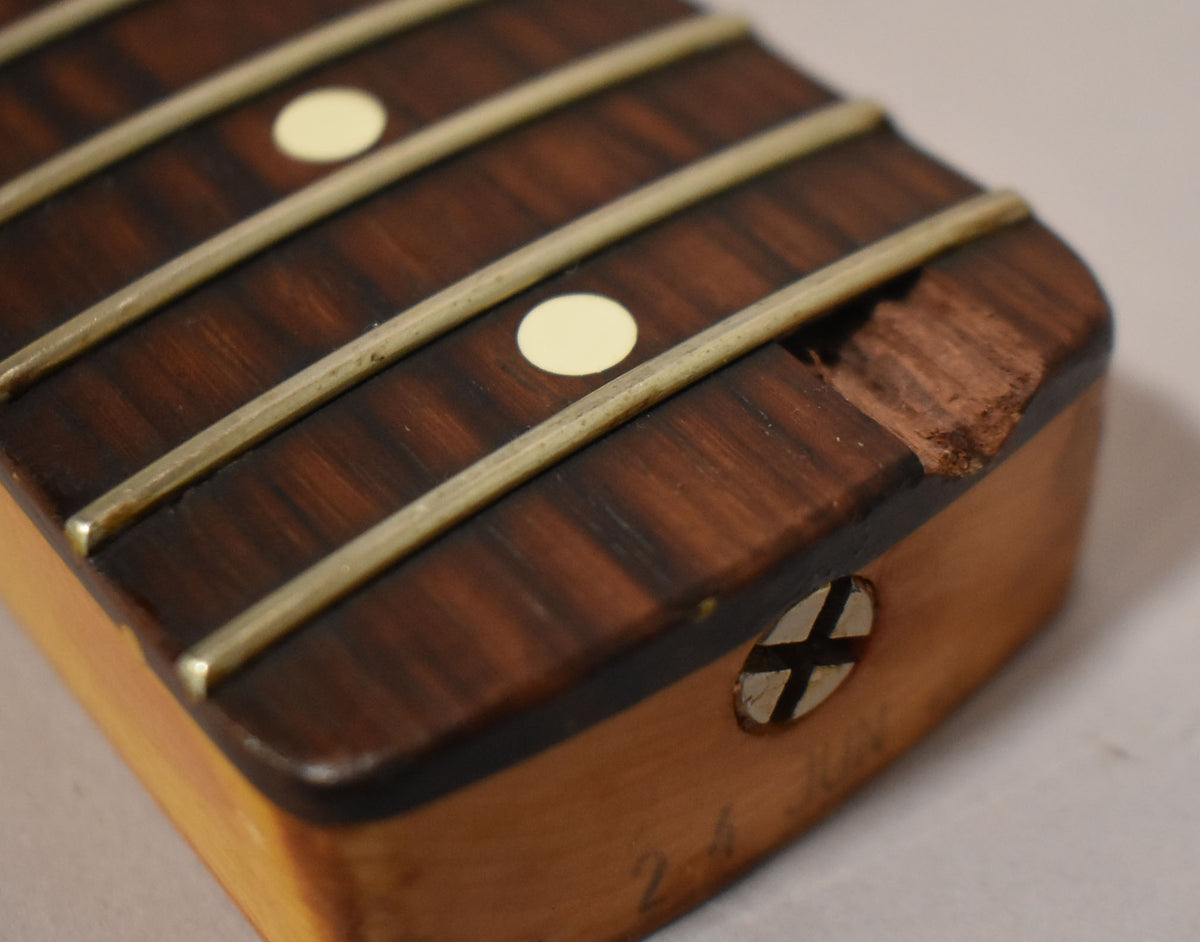 Close-up of a dark rosewood fretboard with cream dot inlays and a large chip on the treble side, showing a truss rod adjustment screw.