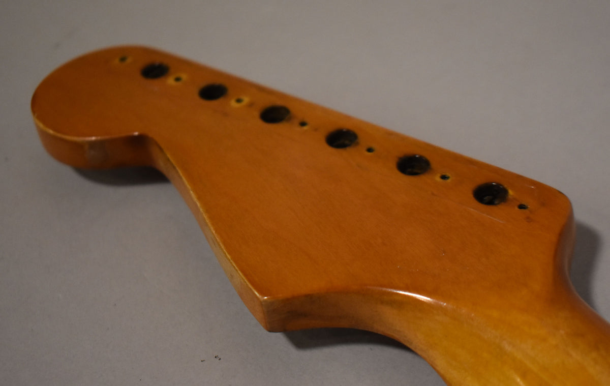 The amber-finished headstock, viewed from above, shows six tuner holes and some finish wear on the edges.