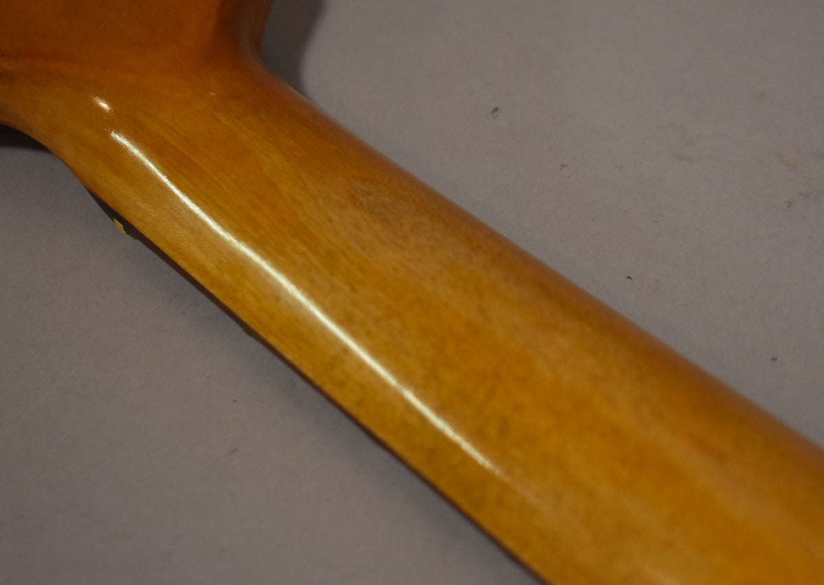 The back of a glossy amber guitar neck is shown at an angle, with visible wear and dark relic marks on the wood.