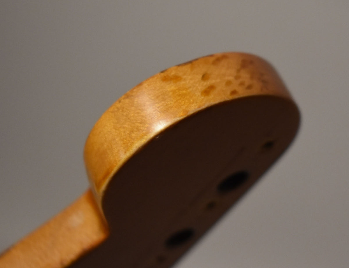 The light brown headstock tip is seen from below, showing dark brown relic wear and two tuner holes on the underside.