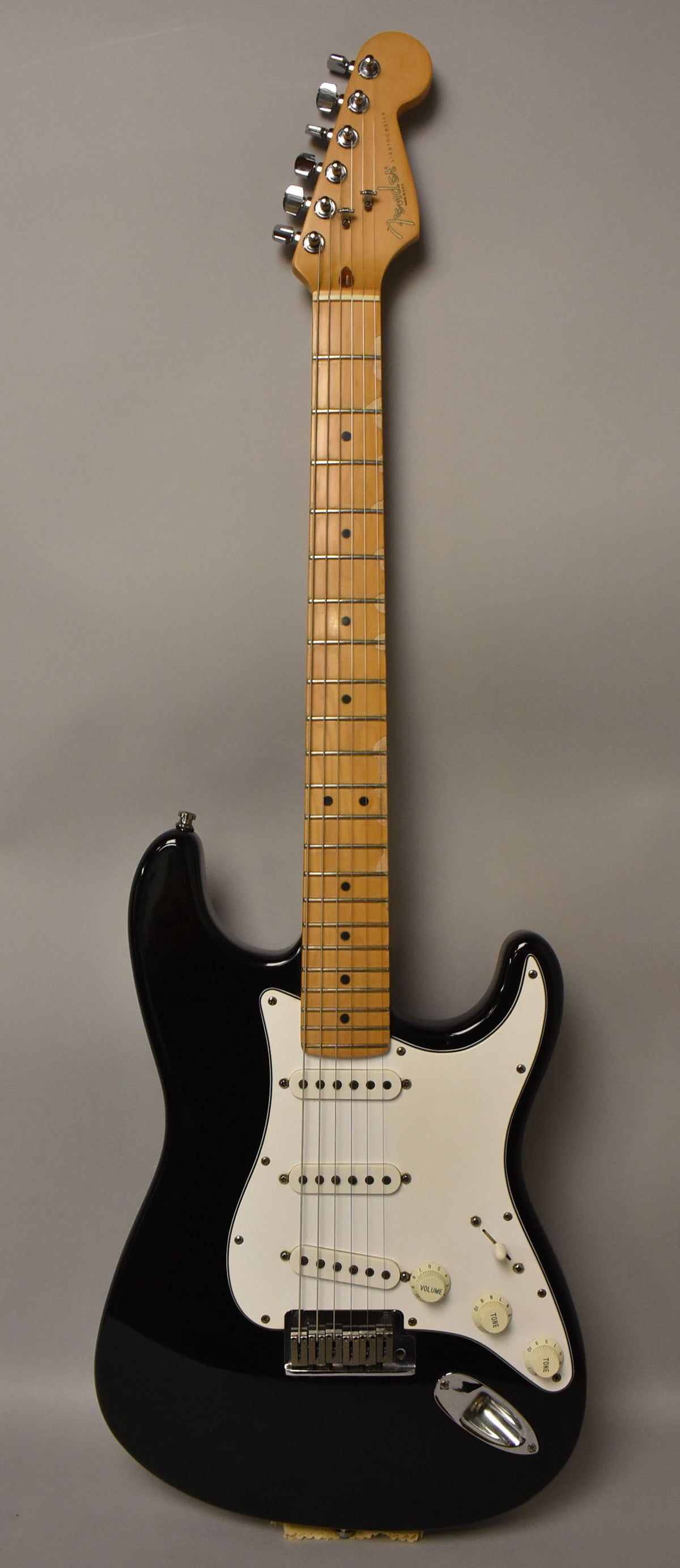 Full-length, front view of a black Stratocaster with a white pickguard, maple neck, and visible wear on the fretboard.