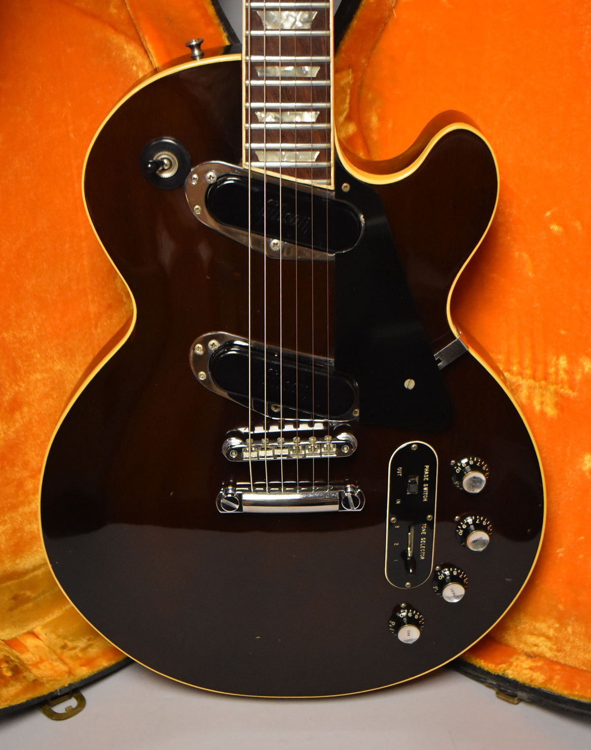 Full view of a dark walnut guitar with a black pickguard, two humbuckers, a chrome bridge, and a unique control plate with switches and four knobs.
