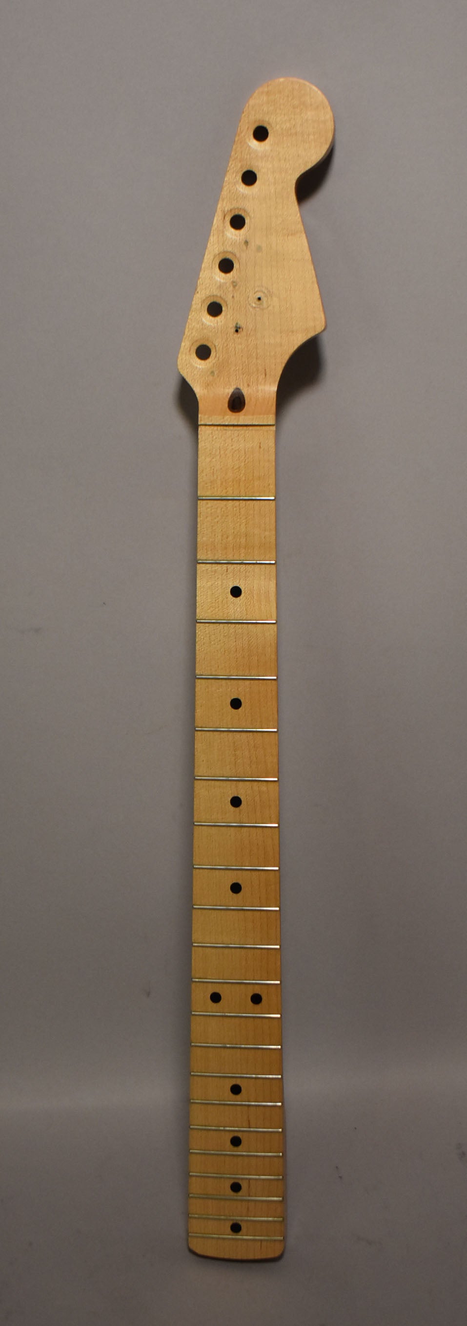 Full-length view of a light maple Stratocaster neck with a natural finish, six tuner holes, and black dot inlays.