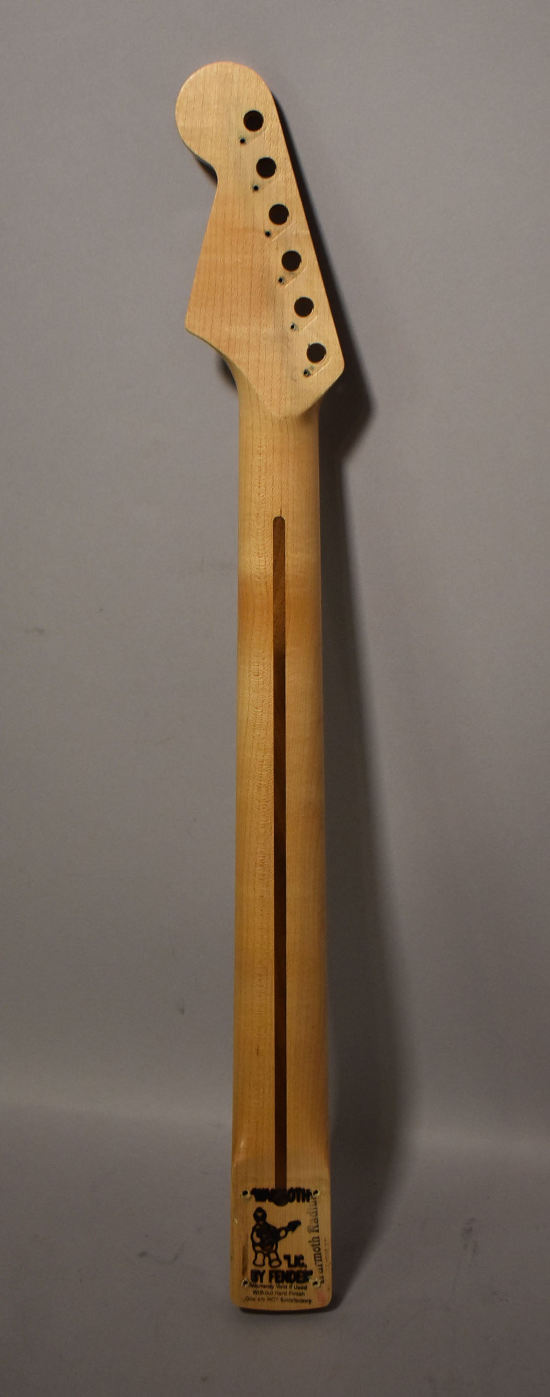 The back of a light maple Stratocaster neck, showing the headstock with six tuner holes and a dark wood skunk stripe.