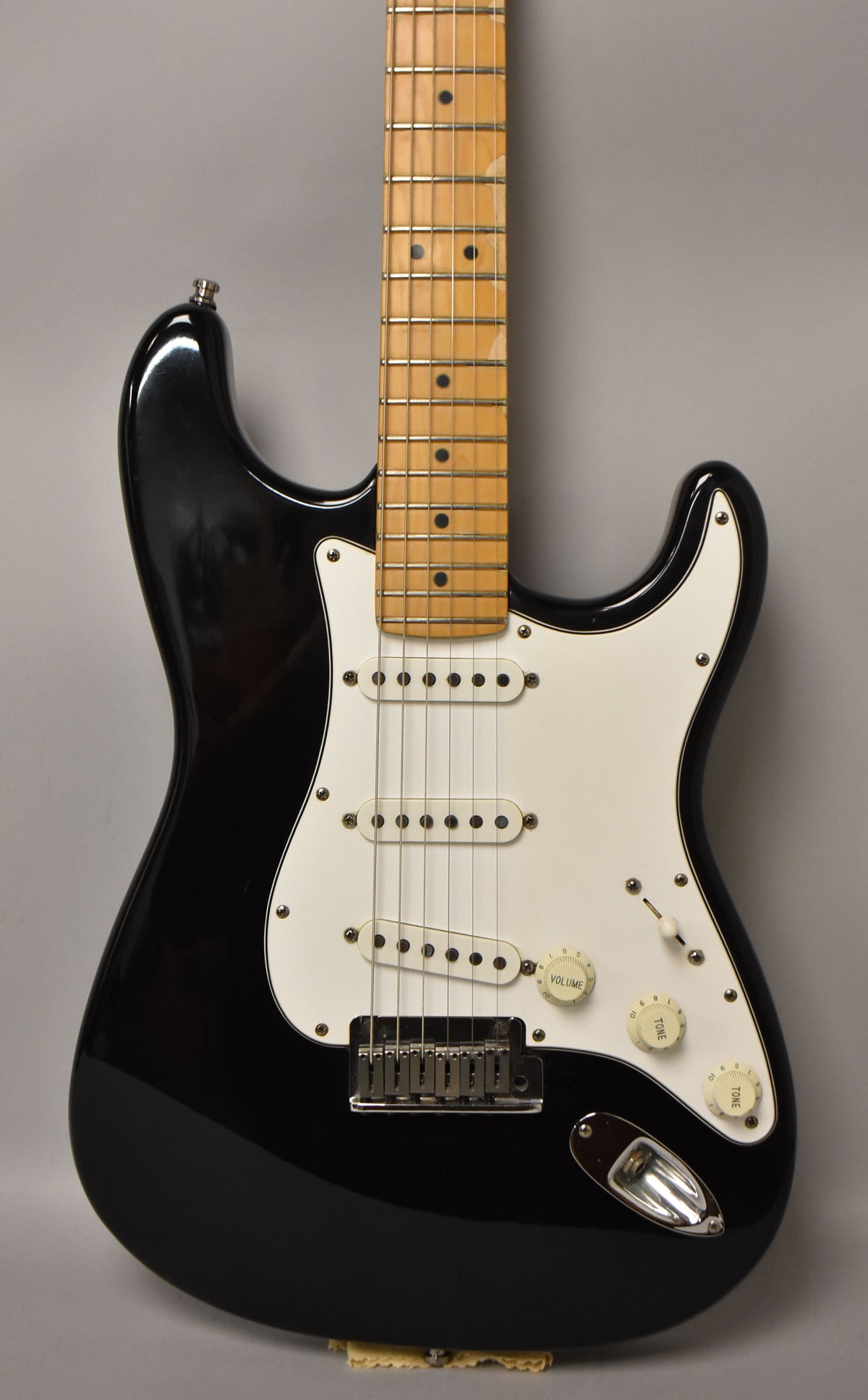 Full-frame, glossy black Stratocaster with a white pickguard, three single-coil pickups, and a maple fretboard with dot inlays.