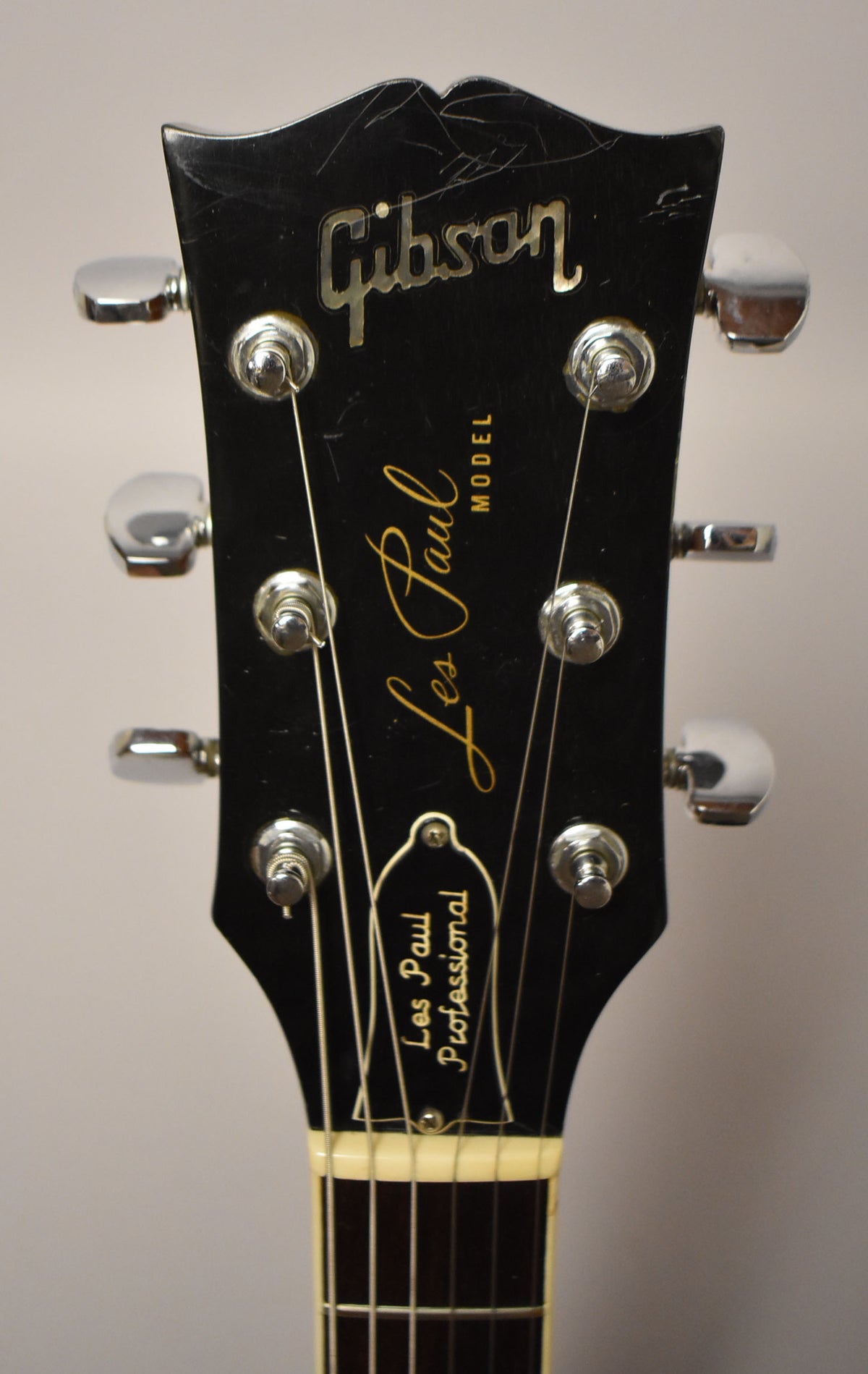 Close-up of the black headstock with chrome tuners, showing finish checking and scratches, and a cream nut.