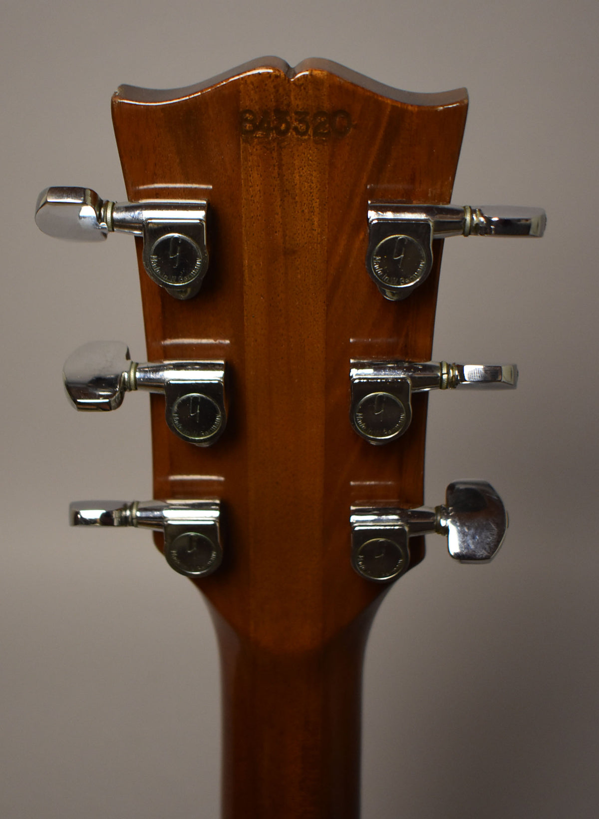 The guitar's headstock, viewed from the back, shows a walnut finish with six chrome tuners and light wear.