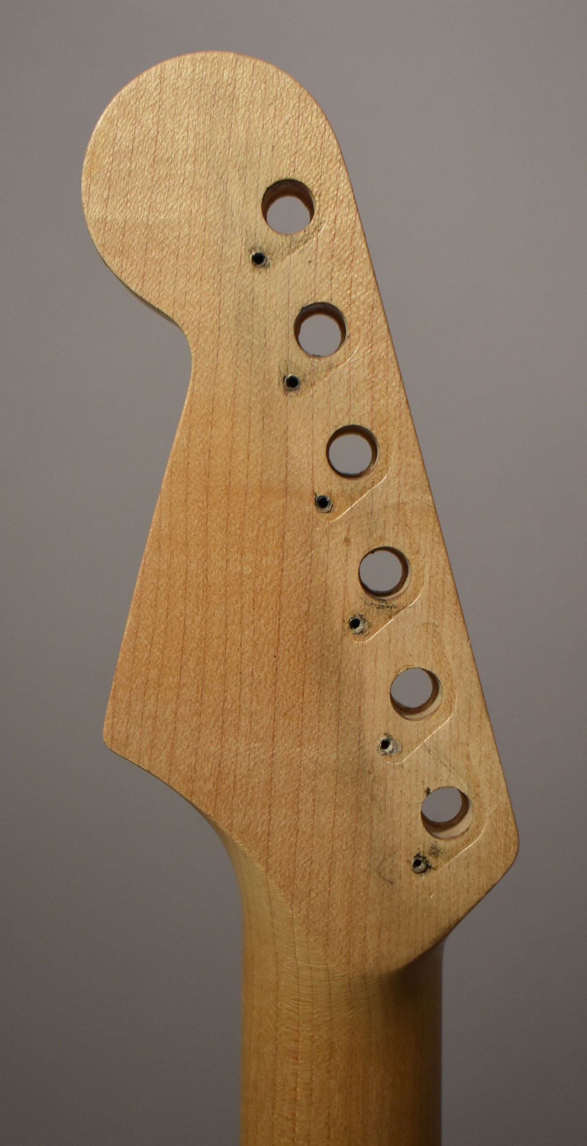 The light-colored maple headstock, viewed from the front, has six tuner holes and small screw holes, with some dark residue around them.