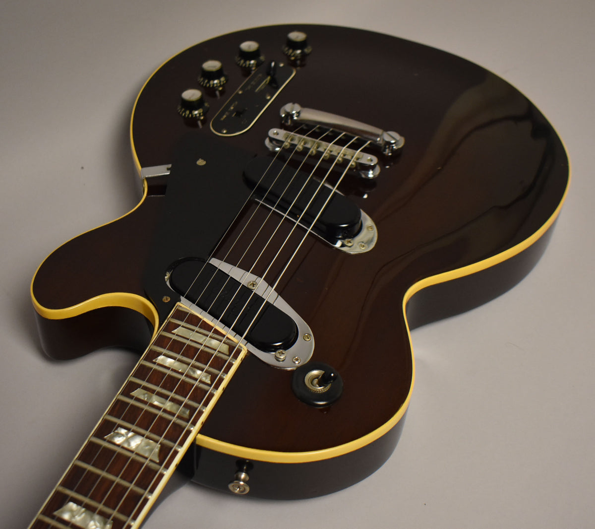 Upper body of a dark walnut electric guitar with cream binding, showing the fretboard, pickups, and control knobs.