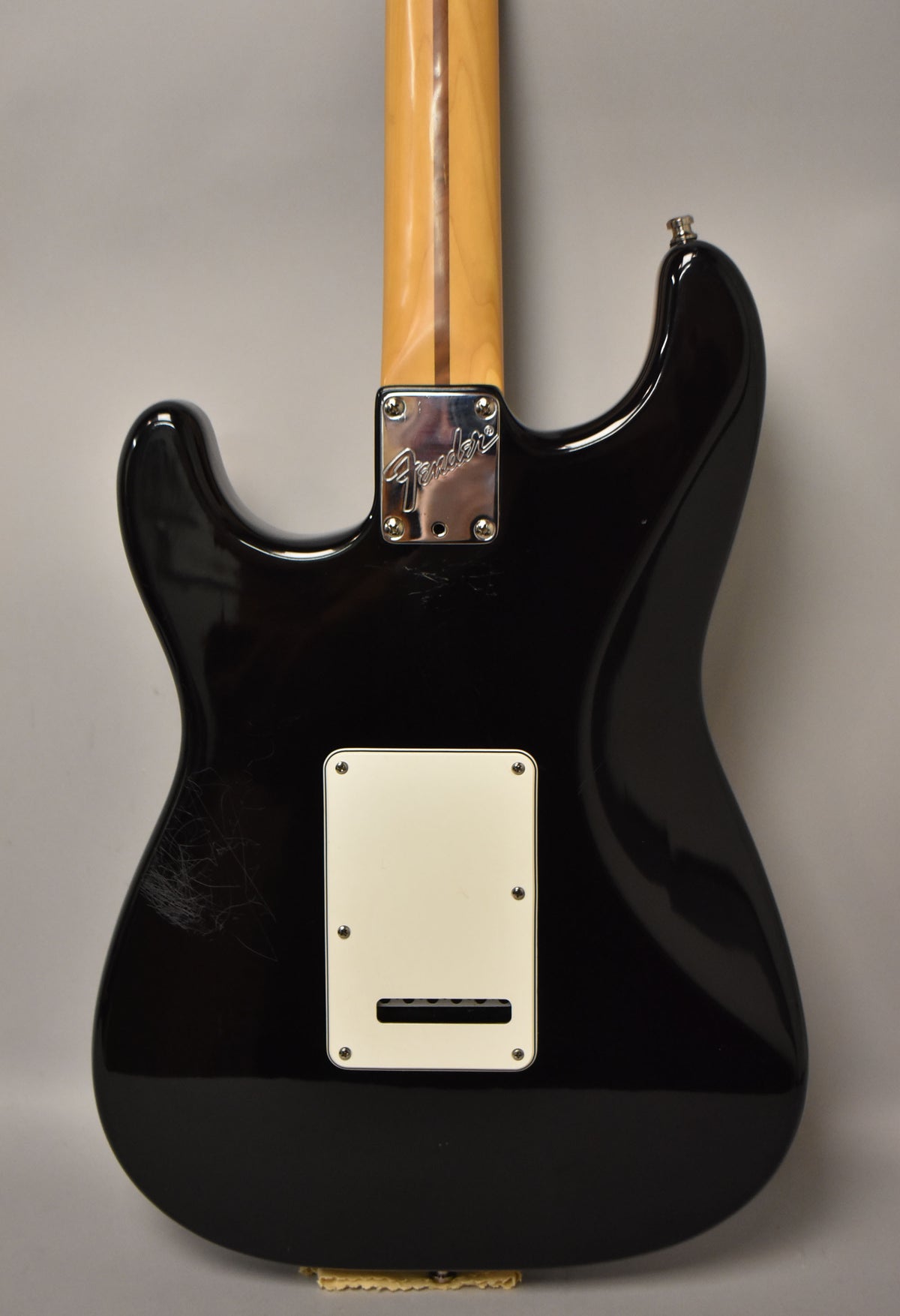 The guitar's glossy black back shows a white tremolo cover, a chrome neck plate, and light scratches on the lower bout.