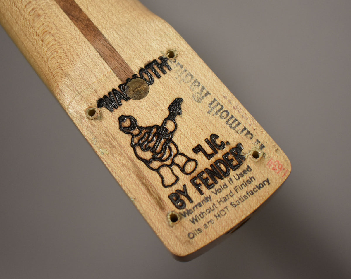 The light maple neck heel shows a dark wood skunk stripe, four screw holes, and black stamped logos and text.
