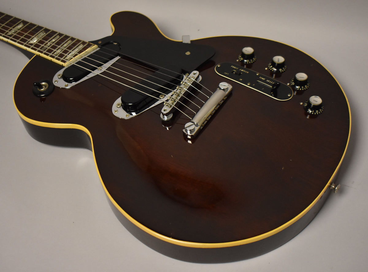 The dark walnut guitar body, with cream binding, shows light wear and features two humbuckers, a tune-o-matic bridge, and five control knobs.