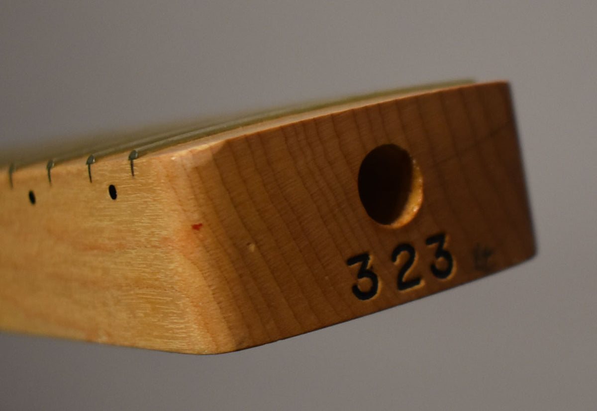 Close-up of the maple neck heel, showing the truss rod adjustment hole and "323" stamped into the wood.