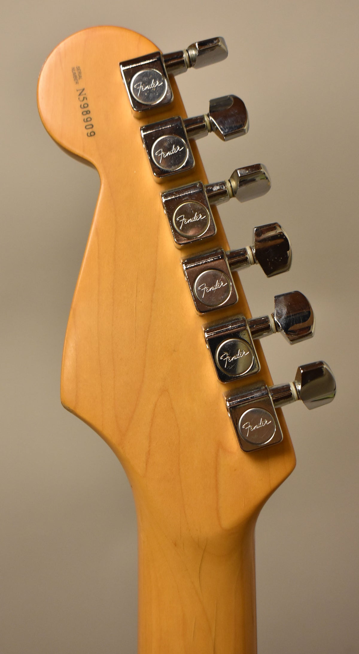 The back of a light maple headstock and neck, showing six chrome tuners with "Fender" stamped on their backs.